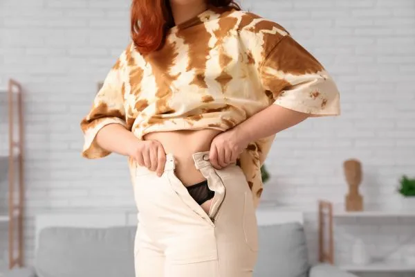 Image of woman trying to do her trousers up after pregnancy weight gain Perth