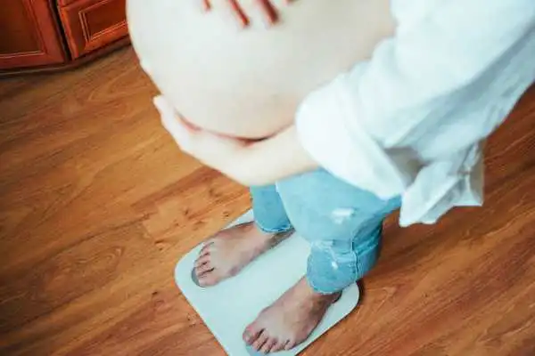 Image of woman weighing herself and experiencing weight gain through pregnancy Perth